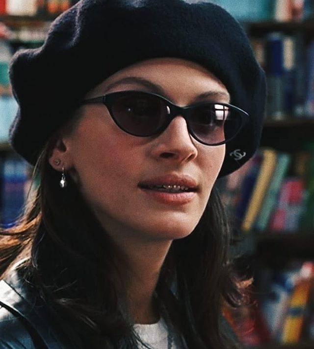 a woman wearing sunglasses and a hat in front of a book shelf with books on it