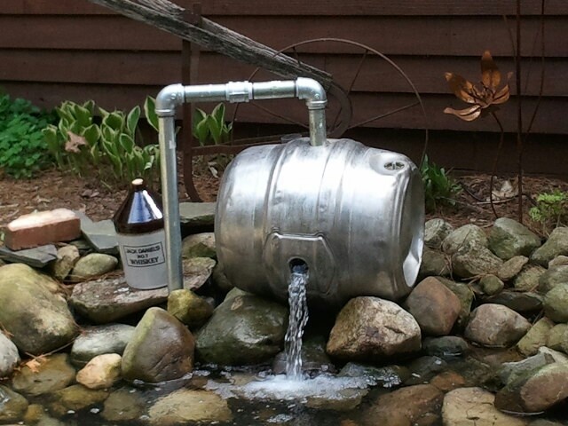 a large metal tank sitting on top of a rock covered ground next to a water fountain