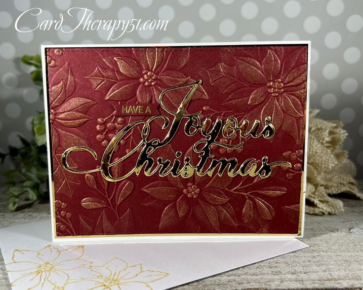 a red christmas card with gold foil lettering on it, and a poinsetti