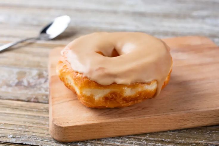 a glazed donut sitting on top of a wooden cutting board