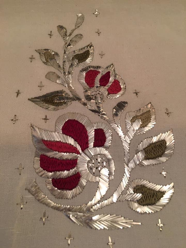 a red and silver flower with leaves on white fabric, next to sequins