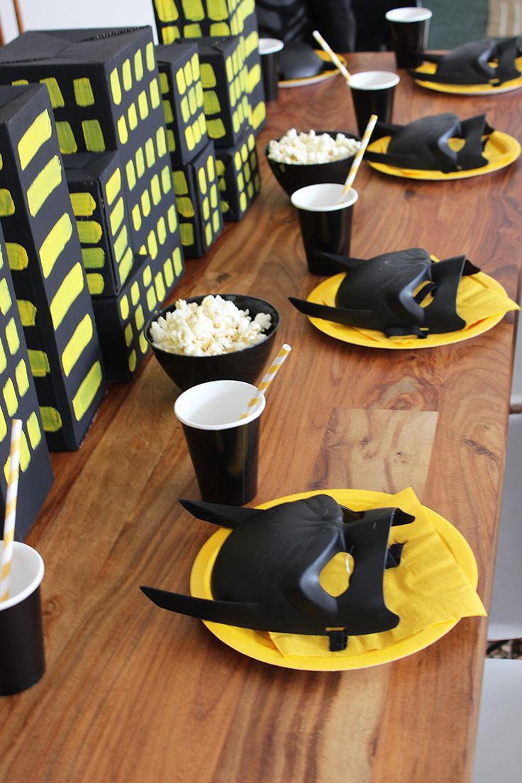 the table is set up with black and yellow paper plates, cups, and napkins