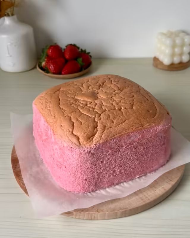 a cake that is sitting on top of a wooden platter with some strawberries in the background