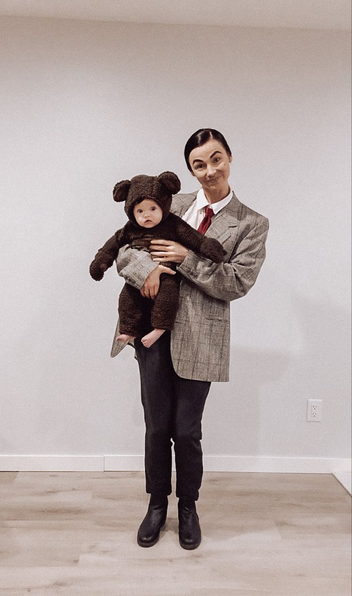 a man in a suit and mask holding a small child with a teddy bear on his chest