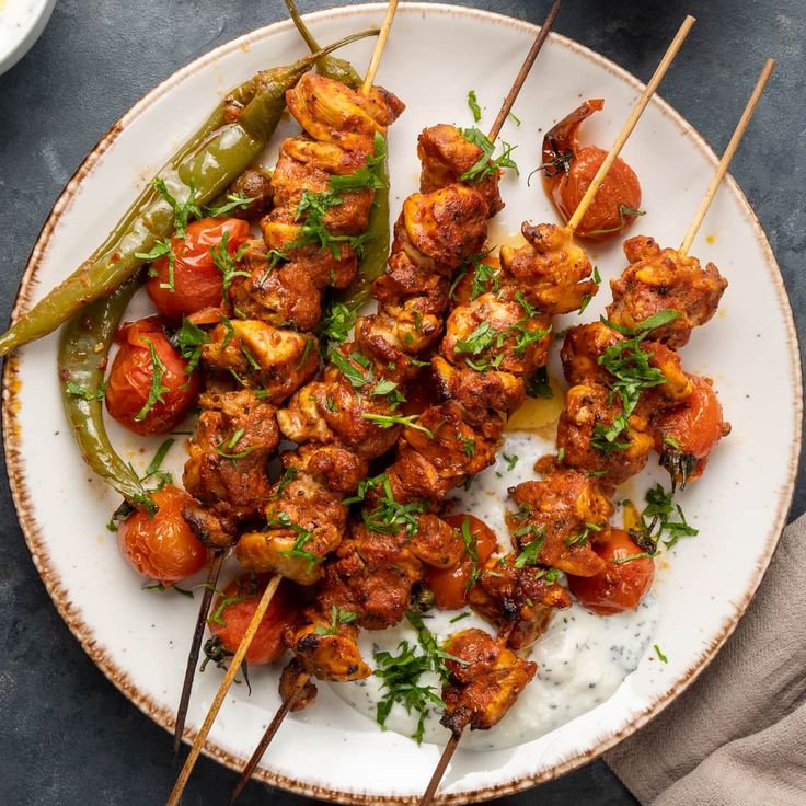 chicken skewers with tomatoes and green peppers on a white plate