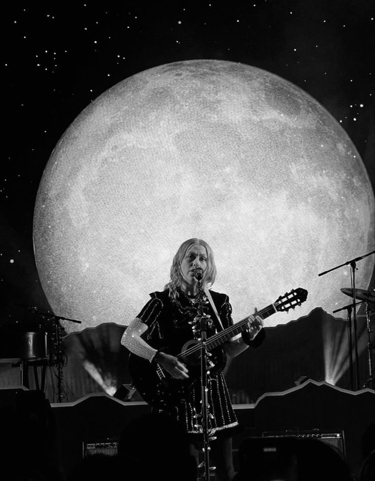 a woman standing on top of a stage holding a guitar in front of a giant moon