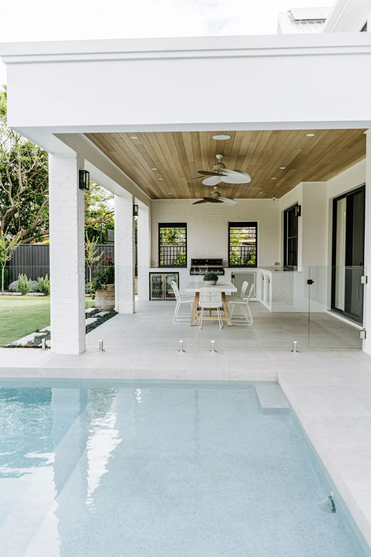 an outdoor dining area next to a pool with a ceiling fan on the roof and sliding glass doors