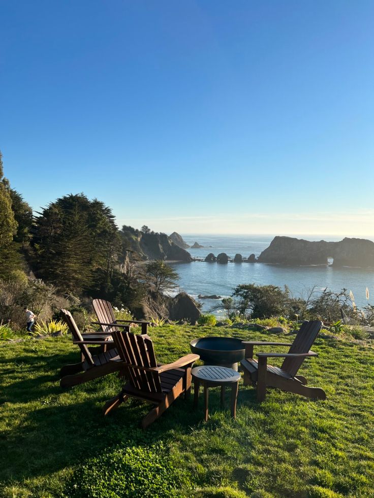 some lawn chairs sitting on top of a lush green field next to the ocean and mountains