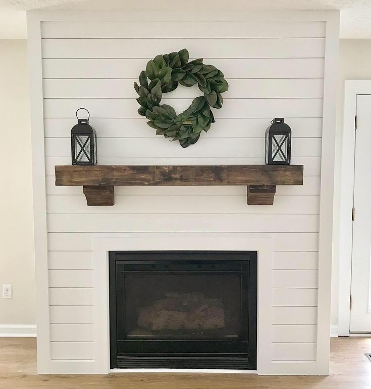 a fireplace with a wreath on the mantle and two lanterns hanging from the mantel