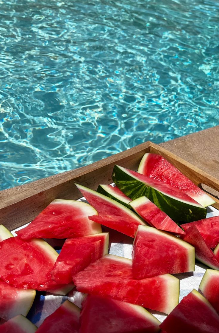 slices of watermelon sit on the edge of a pool next to a swimming board