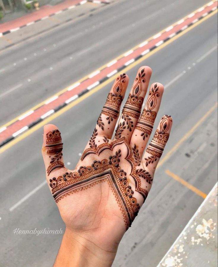 a hand with henna on it near a road and street sign in the background