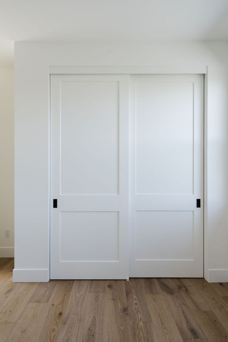 an empty room with white doors and hard wood flooring