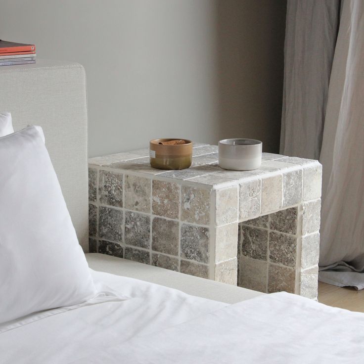 a white bed sitting next to a window with a cup on top of the table