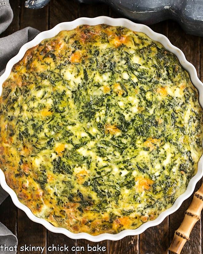 spinach and cheese quiche in a white pie dish on a wooden table next to an oven mitt