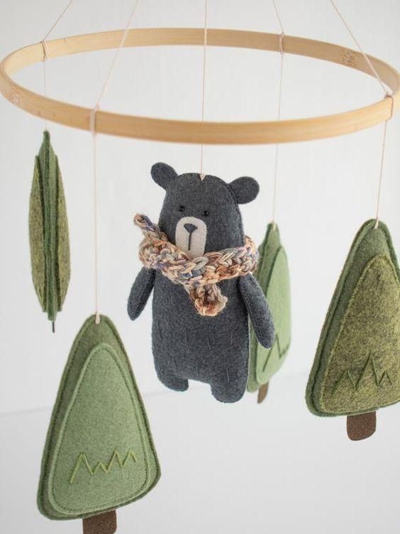 a teddy bear is hanging from a mobile with trees on it's sides and a scarf around its neck