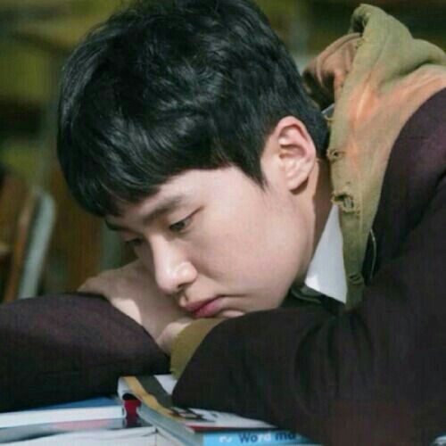 a young man sitting at a table with his head resting on the top of a book