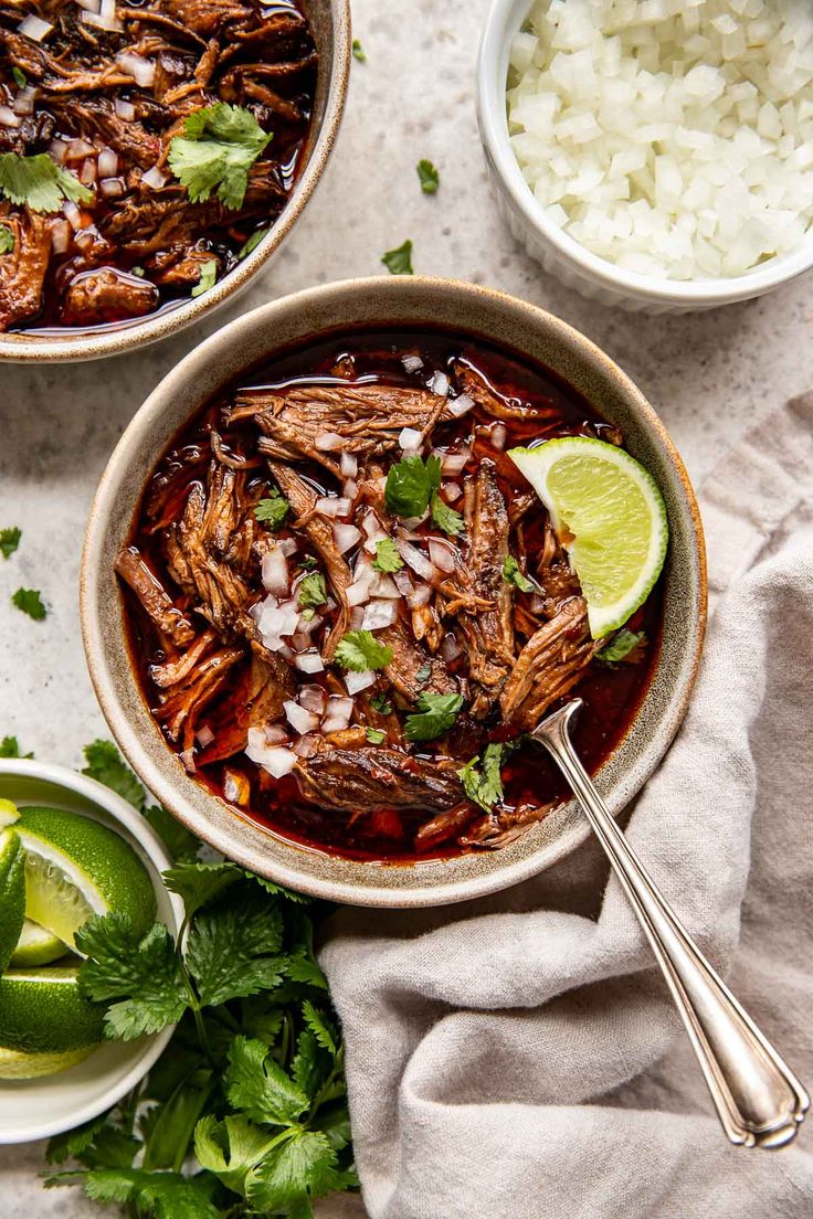 two bowls filled with beef and rice on top of a white cloth next to lime wedges