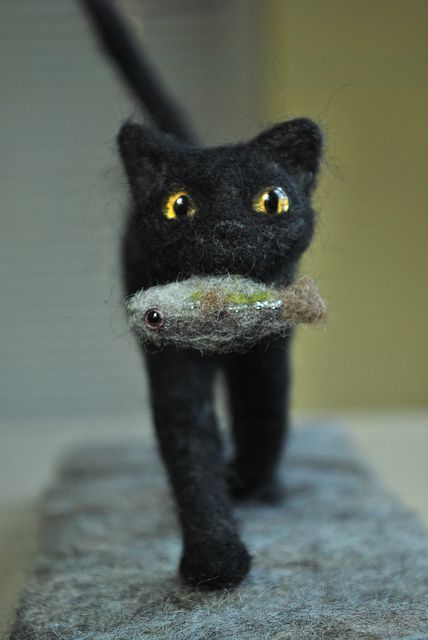 a black cat with yellow eyes is holding a piece of food in it's mouth