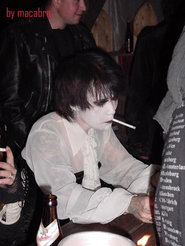 a man with white paint on his face sitting at a table next to a candle