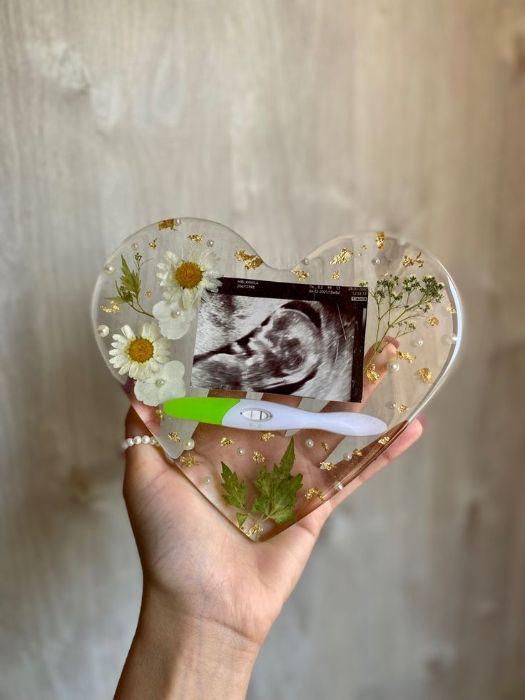 a person holding up a glass heart shaped object with an image of a baby in it