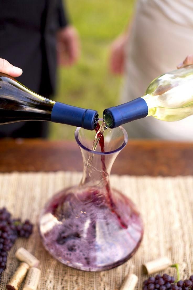 someone pouring wine into a glass with grapes on the table next to it and two people standing in the background