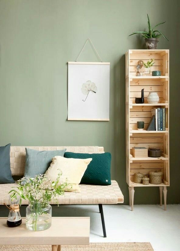 a living room with green walls and white carpeted flooring, a beige sofa is next to a bookcase filled with books