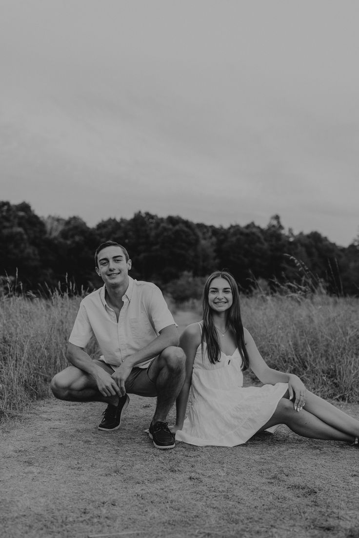 a man and woman sitting on the ground next to each other in black and white