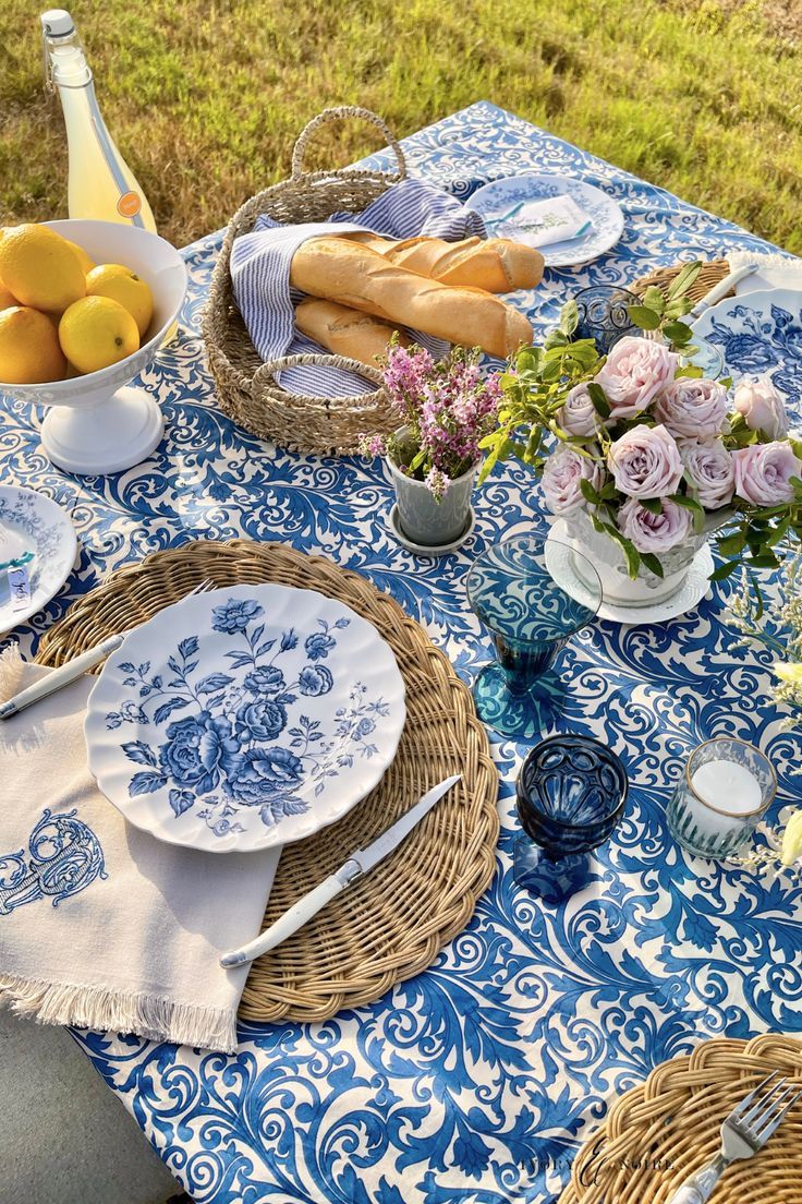 the table is set with blue and white plates, napkins, flowers, lemons and bread