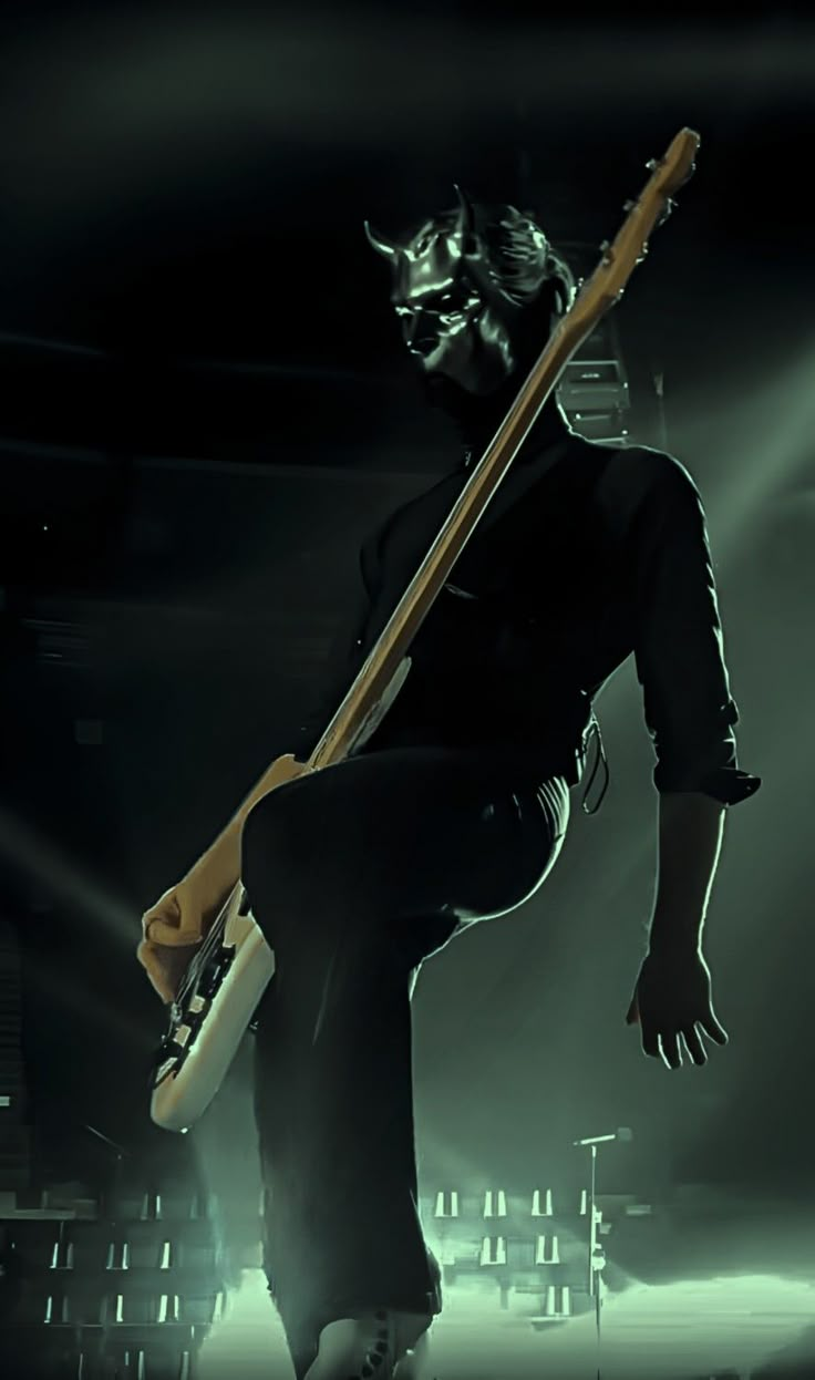 a man holding a guitar in his right hand while standing on stage with lights behind him