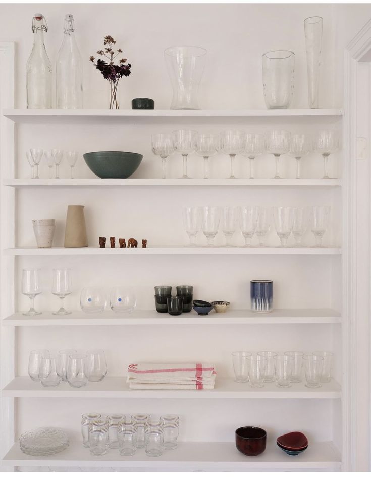 a white shelf filled with lots of glasses and vases on top of each other