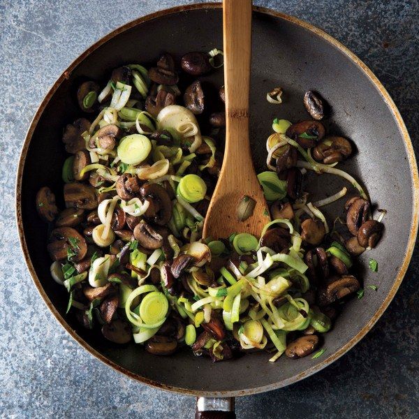 a skillet filled with vegetables on top of a blue countertop next to a wooden spoon