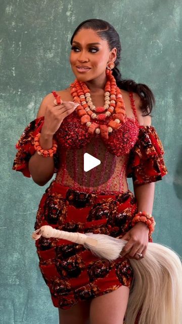 a woman in a red dress is holding a long white horse tail and wearing an orange beaded necklace