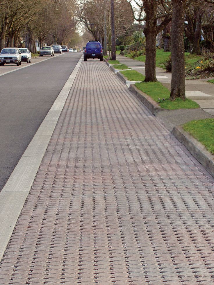 an empty street with cars parked on the side and trees lining the road behind it