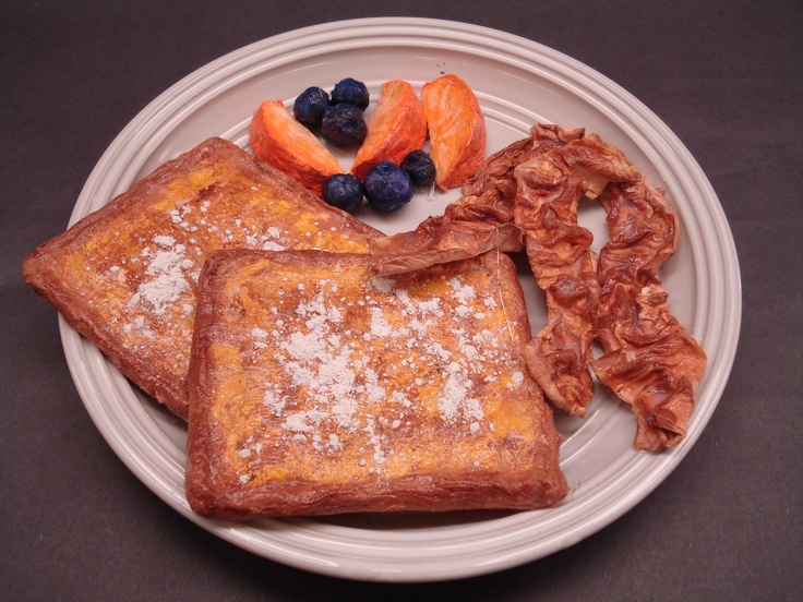 a white plate topped with french toast, fruit and powdered sugar on top of it