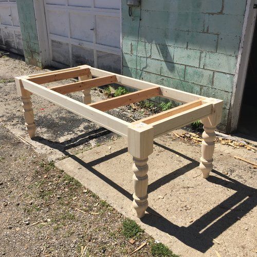 a wooden table sitting on top of a dirt ground next to a building with a garage door