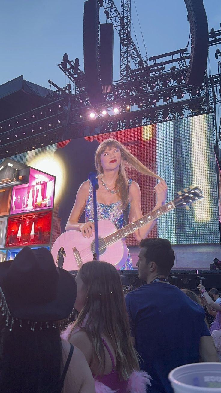 the woman is playing her guitar on stage with other people watching from their seats in front of them