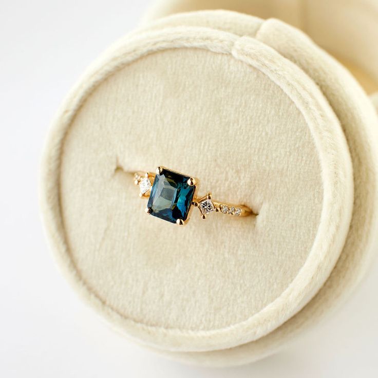 a ring with a blue stone in it sitting on top of a white cloth box