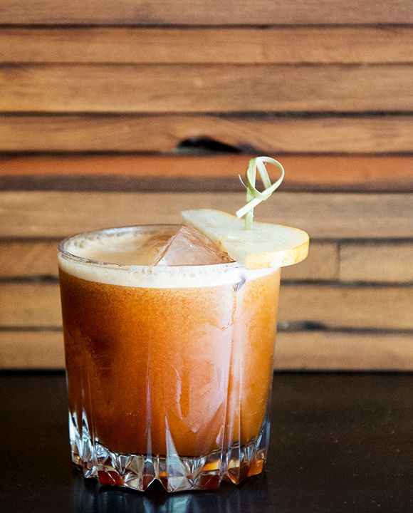 a tall glass filled with ice and topped with an apple slice on top of a table