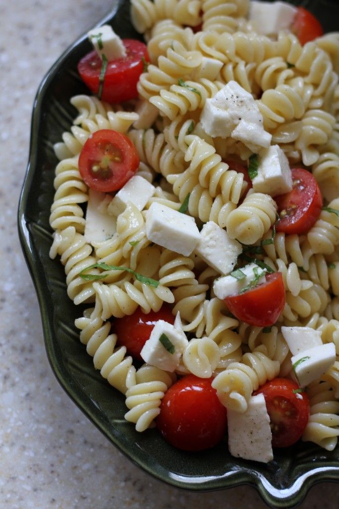 a green bowl filled with pasta salad and feta cheese on top of it's side