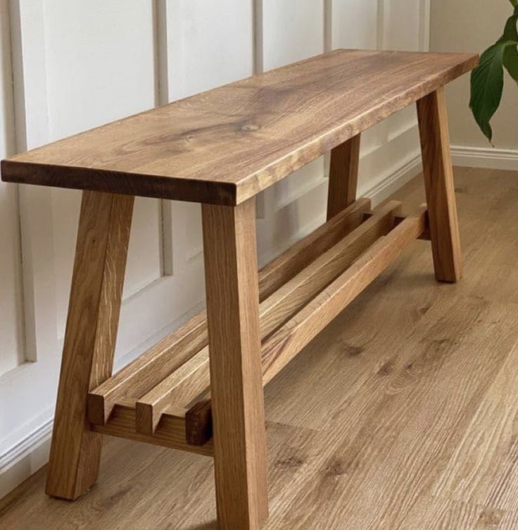 a wooden bench sitting on top of a hard wood floor next to a potted plant