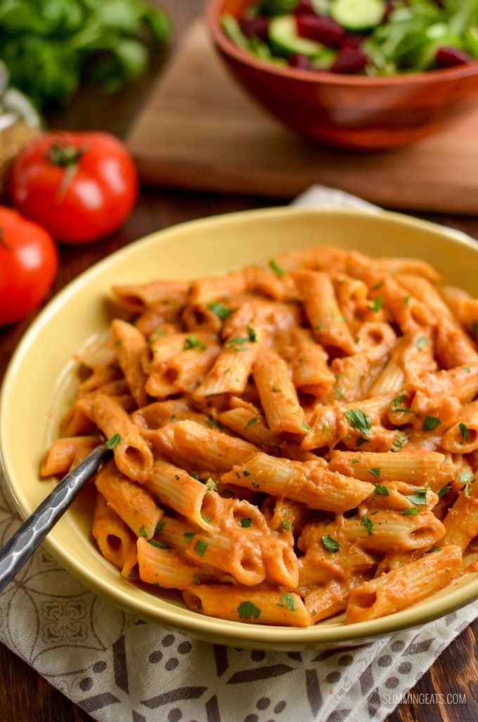 a yellow bowl filled with pasta on top of a table next to tomatoes and lettuce