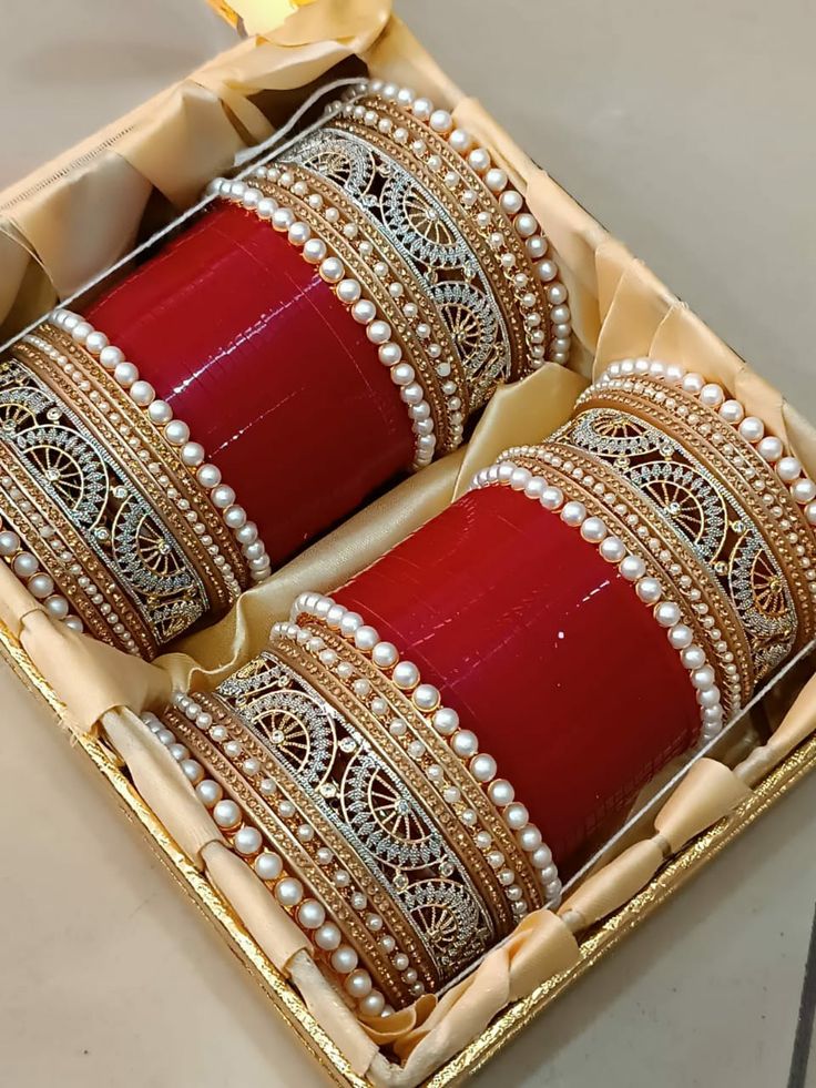 two red bracelets in a box with pearls on the sides and gold trim around them