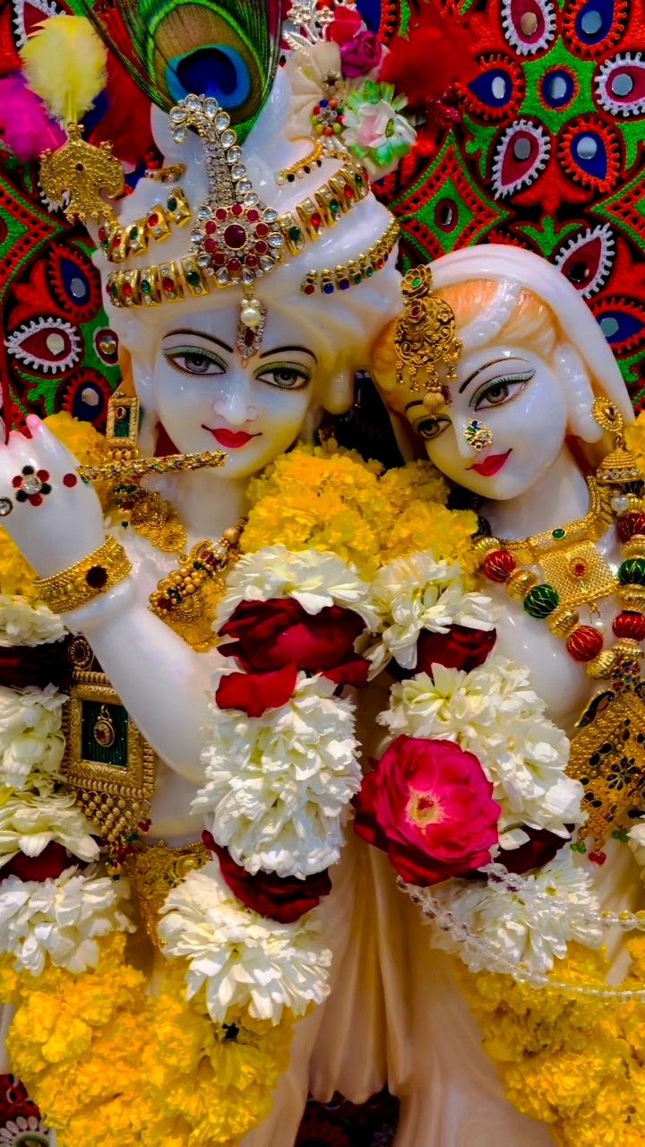 two women dressed in white and yellow costumes with flowers on their heads, one holding a peacock's tail