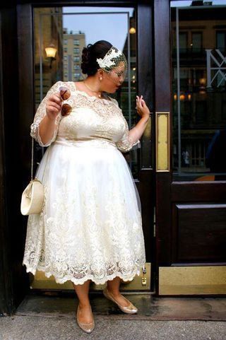 a woman standing in front of a door wearing a white dress and holding a purse