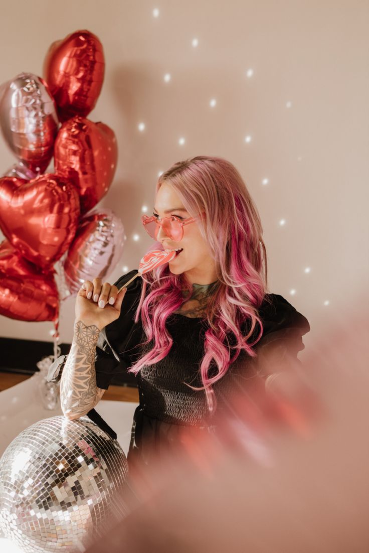 a woman with pink hair is holding some disco balls and balloons in front of her