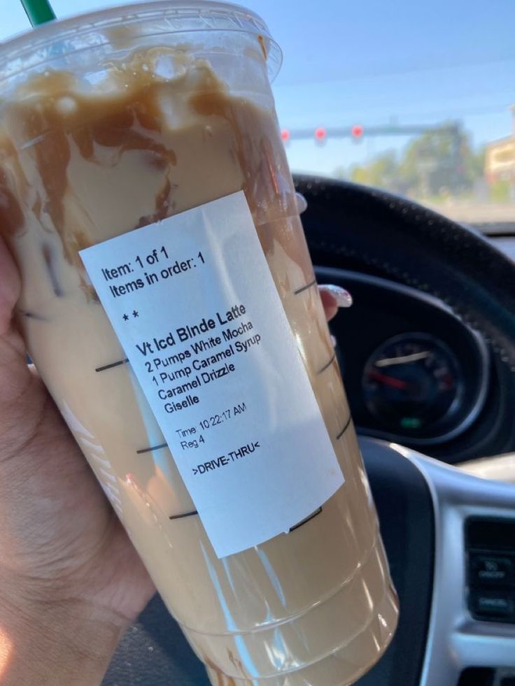 a person holding up a plastic cup filled with liquid in the passenger seat of a car