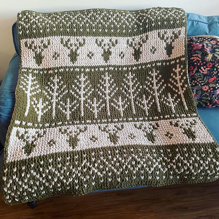 a green and white knitted blanket sitting on top of a blue couch next to pillows