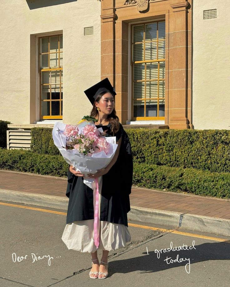 a woman in graduation gown holding a bouquet of flowers on the side of the road