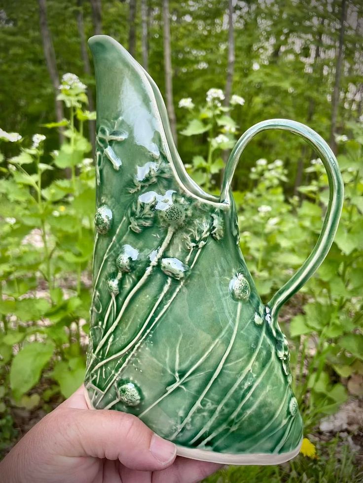 a hand holding up a green vase in the woods