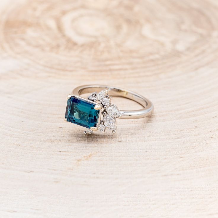 an engagement ring with a blue stone surrounded by white diamonds on a wooden background,